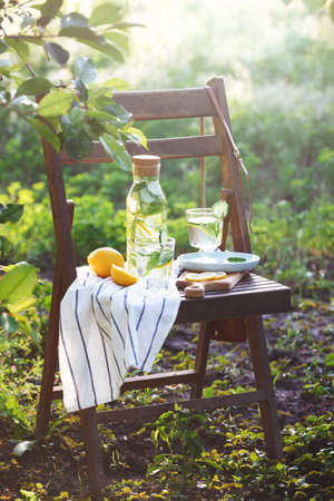 still life - lemonade with lemon, cucumber and mint on a vintage wooden chair in the garden. atmosphere and moodの写真素材