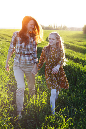 family - happy mother and daughter are walking on a field on the sunset