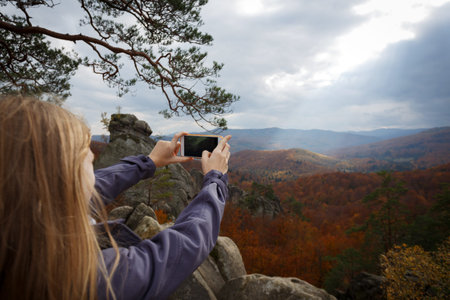 girl stands on Dovbush rocks  taking a photo on a smartphone  at the Carpathians, Ukraineの写真素材