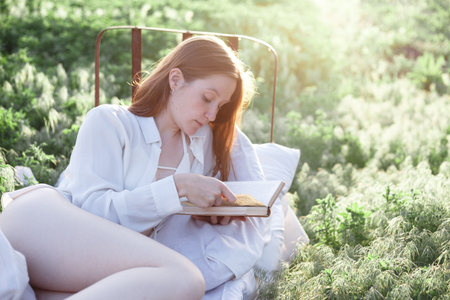 girl reading a book in bed among the fields at sunset