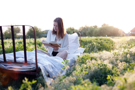 girl reading a book in bed among the fields at sunsetの写真素材