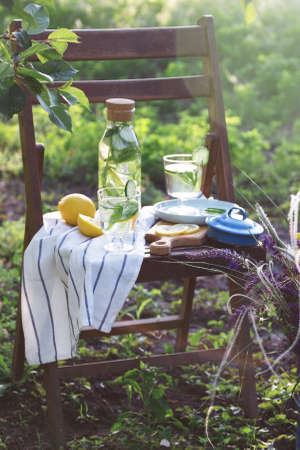 still life - lemonade with lemon, cucumber and mint on a vintage wooden chair in the garden. Milk churn with wild flowers. atmosphere and moodの写真素材