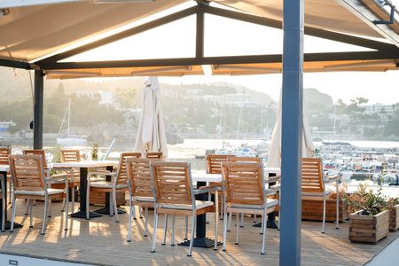 cafe on the waterfront. empty tables, chairs and a bay with boats in the background
