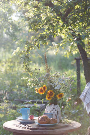 garden and tea party at the country style. still life - cinnamon rolls, cups, dishes and a vase with wildflowersの写真素材