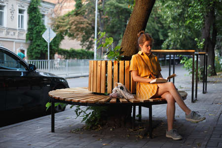 city Style. a girl sits on a bench and reads a bookの写真素材