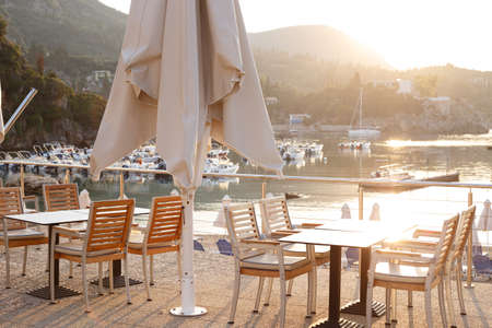 cafe on the waterfront. empty tables, chairs and a bay with boats in the backgroundの写真素材