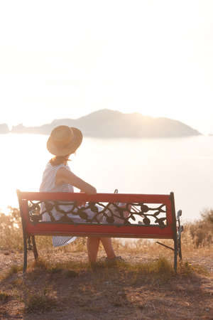 girl tourist sitting on a bench at  the observation deck and looks at the sea and a beautiful landscape On the Sunset, Corfu Island in Greeceの写真素材