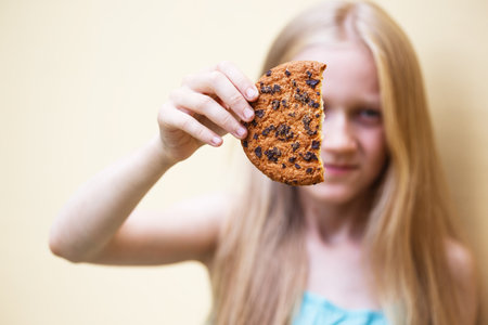 fun young girl eats a big american cookie with chocolateの写真素材
