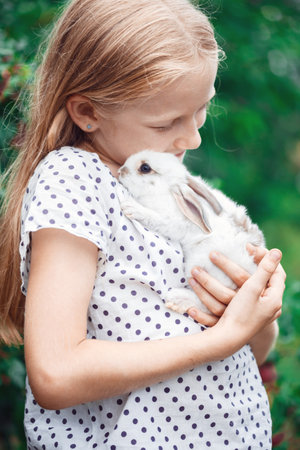 beautiful little girl holding in hands white rabbit at the gardenの写真素材