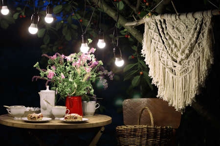tea party in the evening garden. on the table is a vase of flowers, pie with cherry and cup of tea. garland and festive lightingの写真素材
