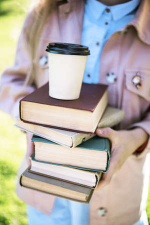 girl holding a stack of books and coffee in her handsの写真素材