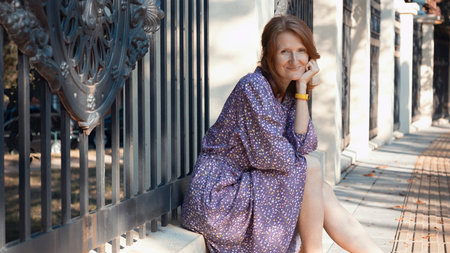 beautiful girl sits on the parapet by the fence in the park