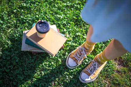a stack of books, glass of coffee and legs in sneakers. learning outdoorsの写真素材