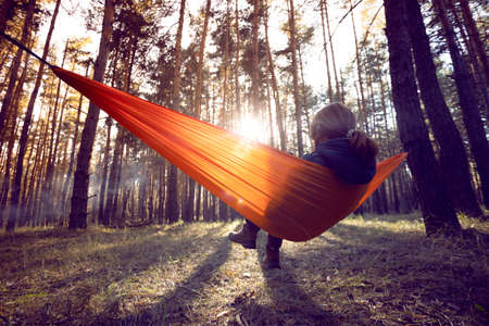 girl sitting in an orange hammock at sunset in the forestの写真素材