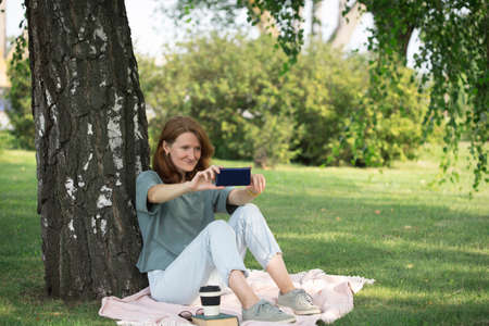 girl sits on the lawn and takes a selfie on the phoneの写真素材
