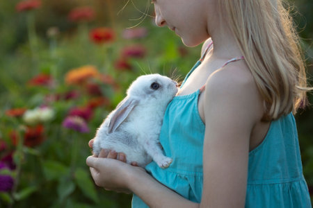 beautiful little girl holding in hands white rabbit at the gardenの写真素材