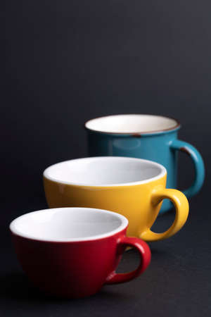 bright ceramics - cups in yellow, blue, red and pink colors on a black backgroundの写真素材