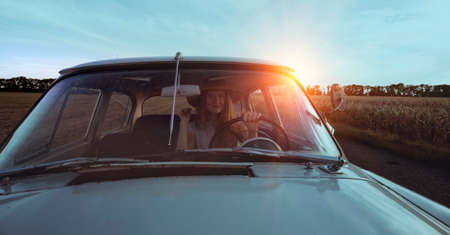 young girl driving a retro car by the road at the fieldsの写真素材