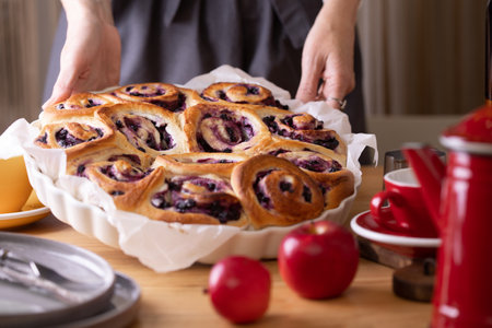 girl in an apron cooking in the kitchen cinnabon buns with cheese cream and  blueberriesの写真素材