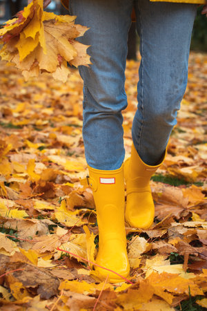 bright autumn. girl in yellow rubber boots walking with a bouquet of maple leavesの写真素材