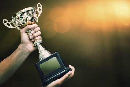 hand holding up a gold trophy cup as a winner in a competitionの写真素材