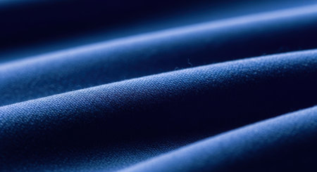 This image showcases a close-up view of a dark blue fabric. The fabric appears to be smooth and has a subtle texture, possibly made of cotton or a similar material. The lighting highlights the folds and waves in the fabric, creating a sense of depth and dimension. The color is rich and deep, adding to the overall aesthetic appeal of the image.の素材