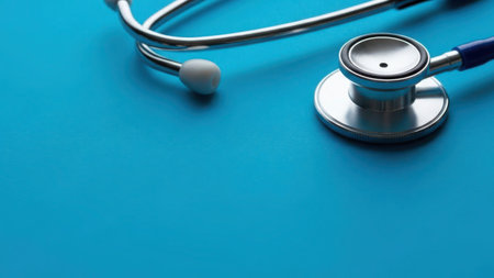 The image depicts a stethoscope resting on a piece of blue fabric. The stethoscope has a silver diaphragm and earpieces, with one earpiece colored white and the other colored blue. The background is a solid blue fabric, providing a clean and professional setting. This image is commonly associated with medical professionals and healthcare.の素材
