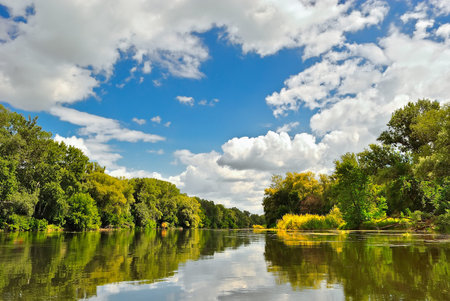Beautiful river with wooded banks under blue cloudy sky