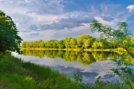 Quiet summer evening on the banks of the picturesque river under cloudy skyの写真素材
