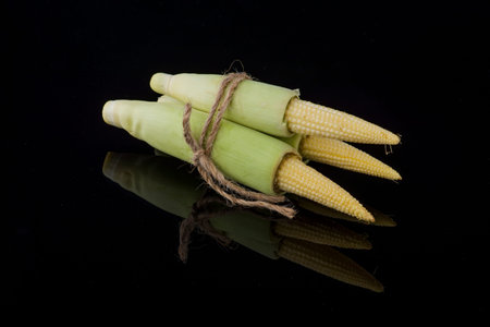 Young raw baby corn isolated on black background with small reflection
