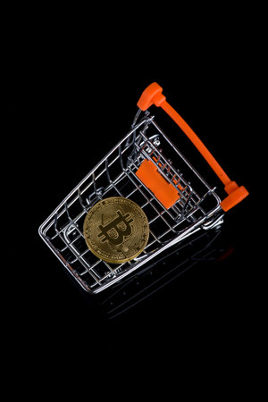 Bitcoin on mini shopping cart isolated on black background. Reflection on glassの写真素材