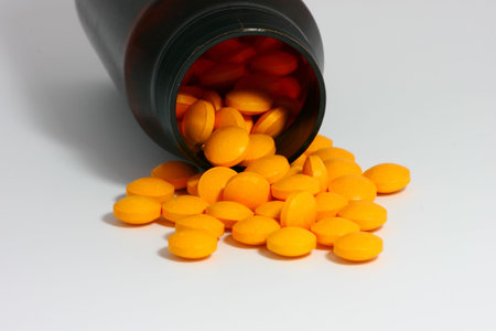 orange vitamins pills and dark amber bottle on white background