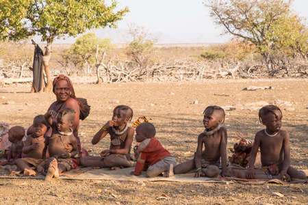 KUNENE, NAMIBIA - SEPTEMBER 22, 2013: A Himba women and children sitting on a blanket in their village.のeditorial素材