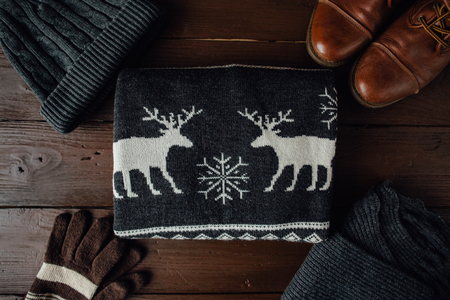 Men's winter clothes on a brown wooden table. Winter shoes, sweater with deer, knitted scarf and hat, gloves. Top viewの写真素材