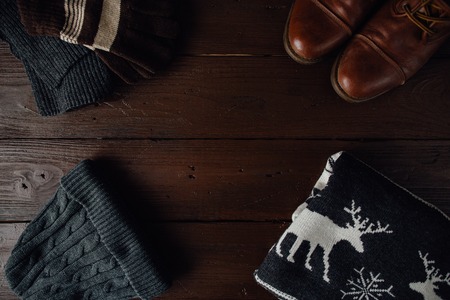 Men's winter clothes on a brown rustic background. Winter shoes, sweater with deer, knitted scarf and hat, gloves. Top viewの写真素材