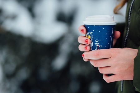 Coffee outdoors. Girl holds coffee in hands in winter cold day. Coffee in hands closeupの写真素材
