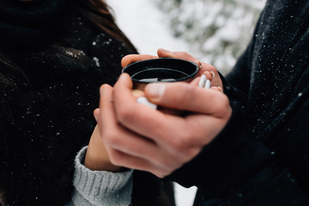 Hands of couple in love holding cup of hot tea in cold winter dayの写真素材