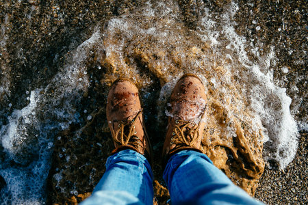 Top view on brown men's boots on the stone beach, wave. Sea stones background.