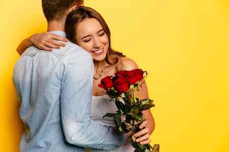 Attractive smiling woman hugging her boyfriend, after getting red bouquet of roses. St. Valentine's day.の写真素材