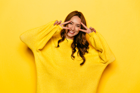 Happy pretty girl with curly hair posing at camera showing peace sign. Valentine's day.の写真素材