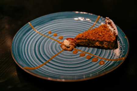 Piece of chocolate cream cake with caramel and powdered sugar on plate. Modern presentation.