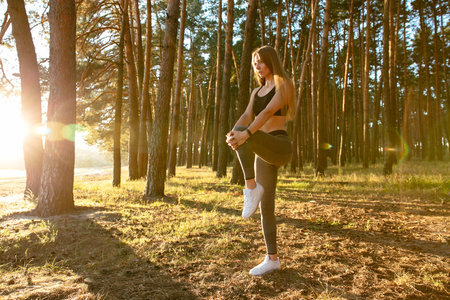 Full length view of gorgeous female runner doing stretching exercise, workout in the wood in the...