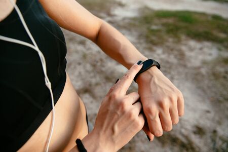 Young female checking the time on her watches after running, outdoors, listening to music in headphones. Workout concept. Close-up view.の写真素材
