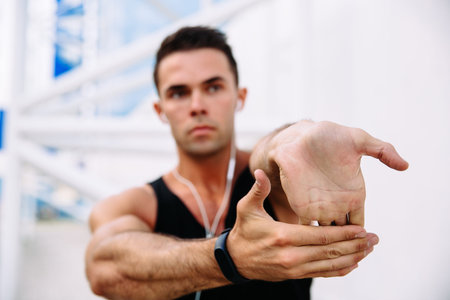 Athlete male in earphones while stretching his arms, preparing to workout outdoors. Sport concept.