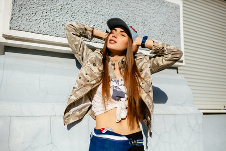 Trendy young woman with long hair enjoying the sunny day, holding her head with both of hands,...