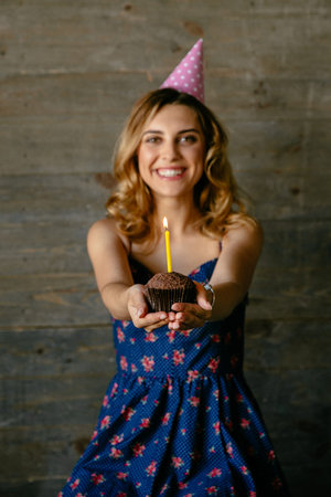 Happy attractive girl holds a chocolate cupcake with candle, celebrating her birthday, has a fun....