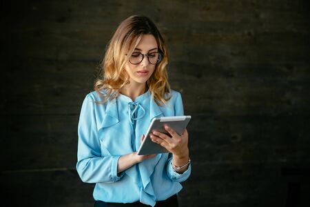 Charming young business woman working on tablet, wearing eyeglasses. Dressed in blue blouse.の写真素材