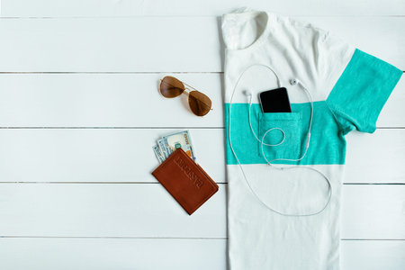 Men's summer t-shirt with passport, money, sunglasses  and mobile phone with headphones on white...