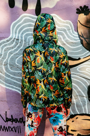 A view from the back of the girl in hood, dressed in colorful green jacket and bright pants,...