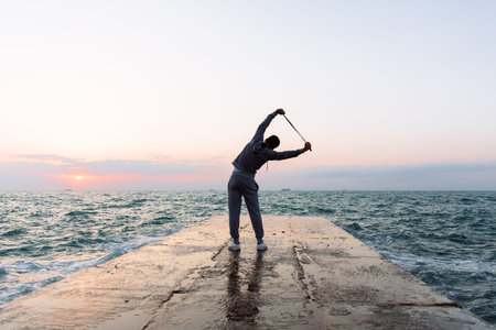 Full length photo of sportsman practicing exercises, stretching with skipping rope, standing on...